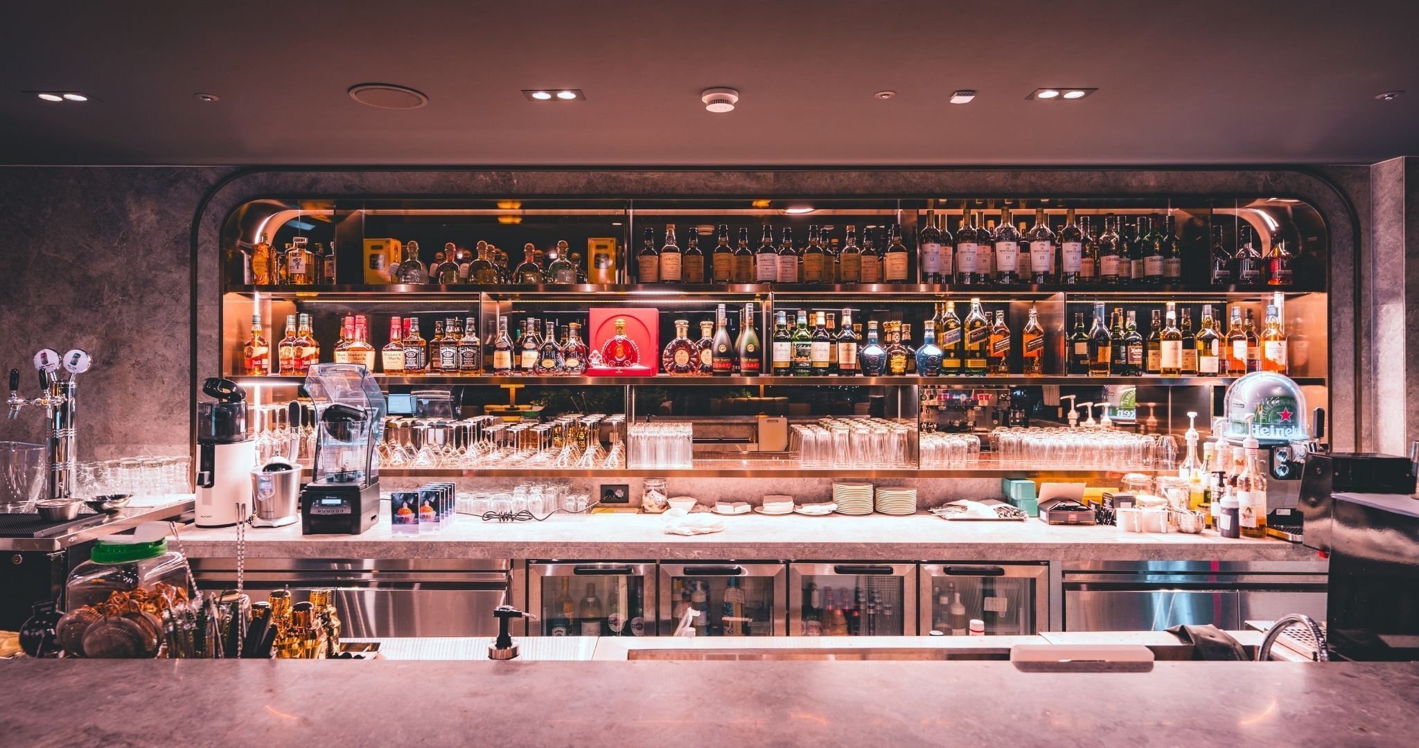 Una barra con varias estanterías llenas de botellas de licores, una máquina de café y distintos utensilios de bar.