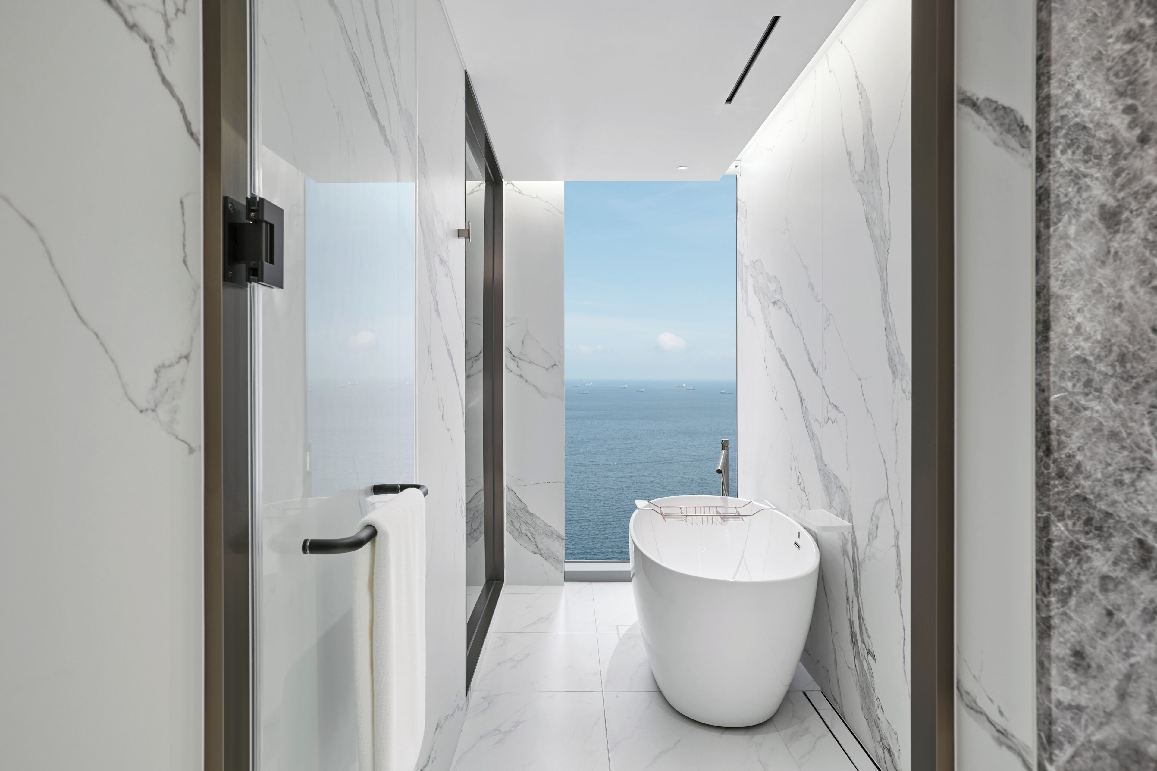 Un baño moderno con bañera, vistas al mar y paredes de mármol.