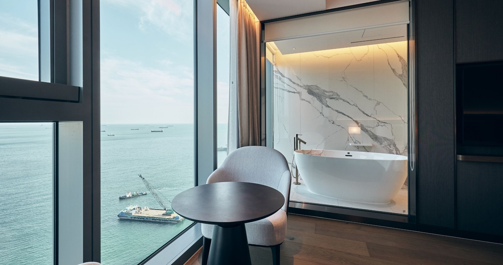 Un baño moderno con una bañera independiente, un ventanal grande con vista al mar y barcos.