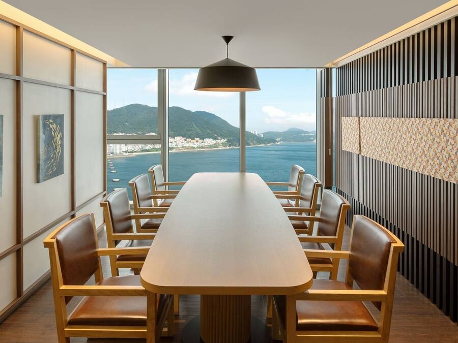 Un salón de conferencias con una larga mesa, sillas de madera y vistas al mar y a las montañas.