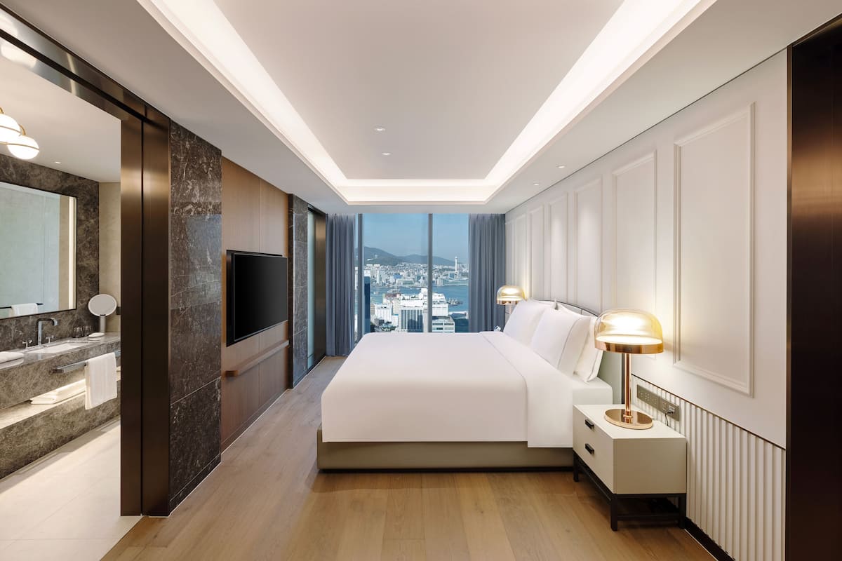 Ein modernes Hotelzimmer mit einem großen Bett, einem Fernseher, einem Badezimmer mit Waschtisch und Blick auf die Stadt.