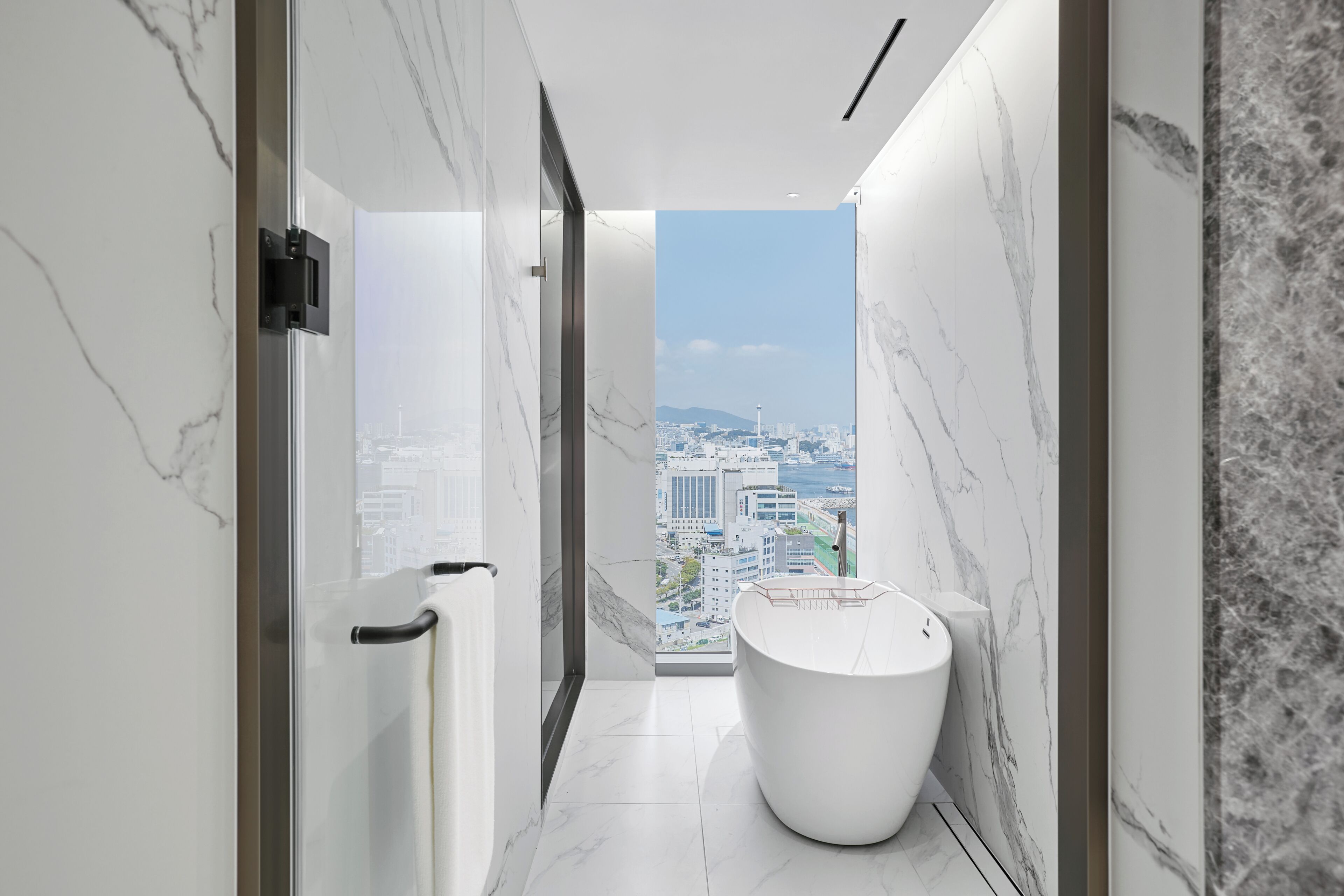 Un baño moderno con bañera, vistas a la ciudad y paredes de mármol.