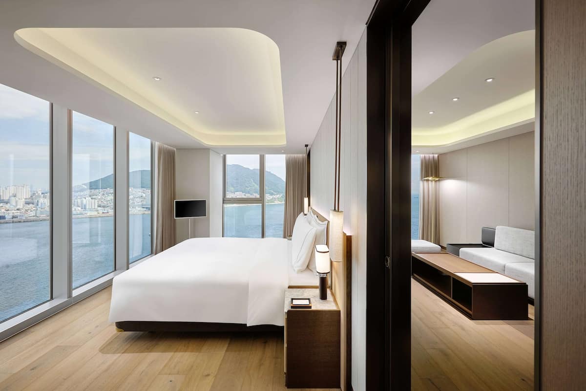 Ein modernes Hotelzimmer mit einem großen Bett, Nachttischen, einem Fernseher und Blick auf Stadt und Wasser.