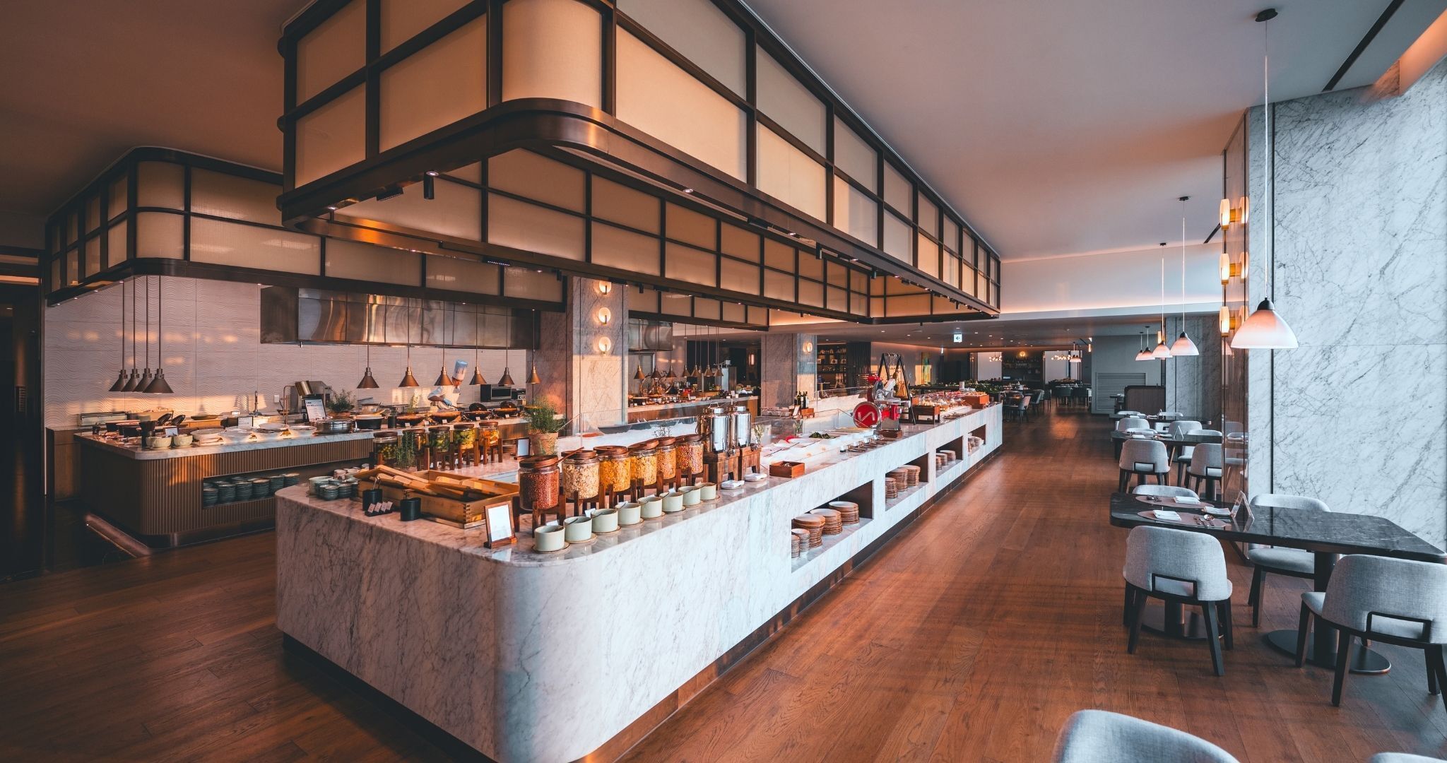 A modern restaurant with a central bar area, wooden flooring, and marble walls.