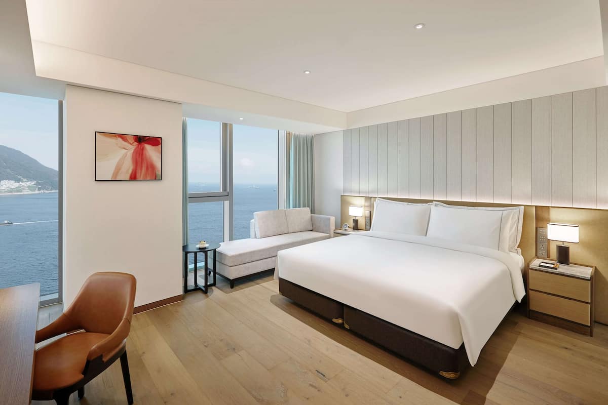 Ein modernes Hotelzimmer mit einem großen Bett, einer Sitzecke mit Meerblick und einem Schreibtisch mit Stuhl.