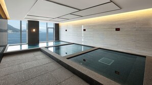 A modern indoor swimming pool with clear glass walls, a tiled floor, and a digital display showing the water temperature. - Wyndham Grand Busan Ijin (Busan)