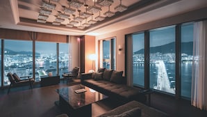 A spacious living room with a large sofa, a coffee table, and a floor lamp. The room features large windows with a city view and a modern chandelier. - Wyndham Grand Busan Ijin (Busan)