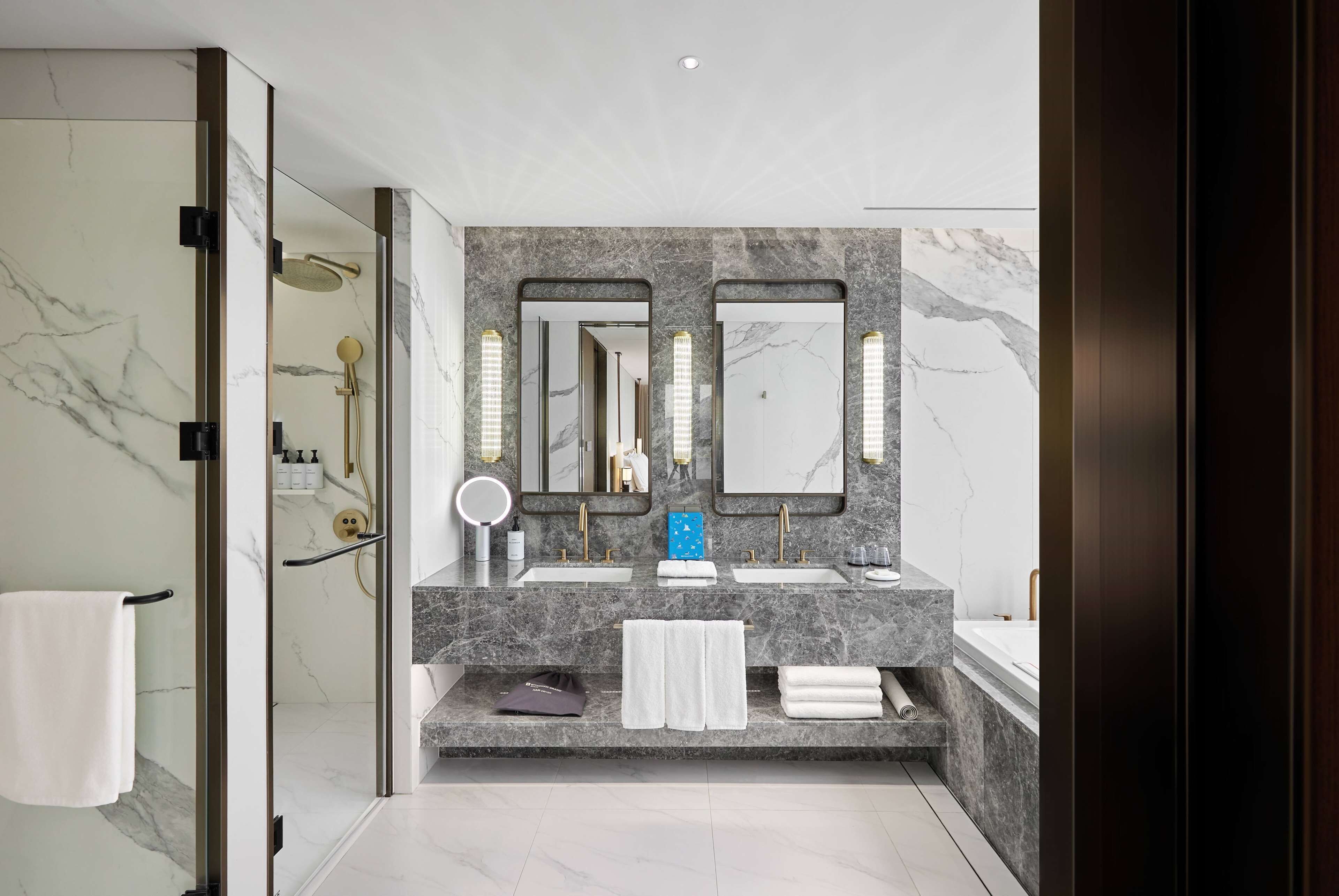 A modern bathroom with a glass shower enclosure, marble countertops, dual sinks, and large mirrors.