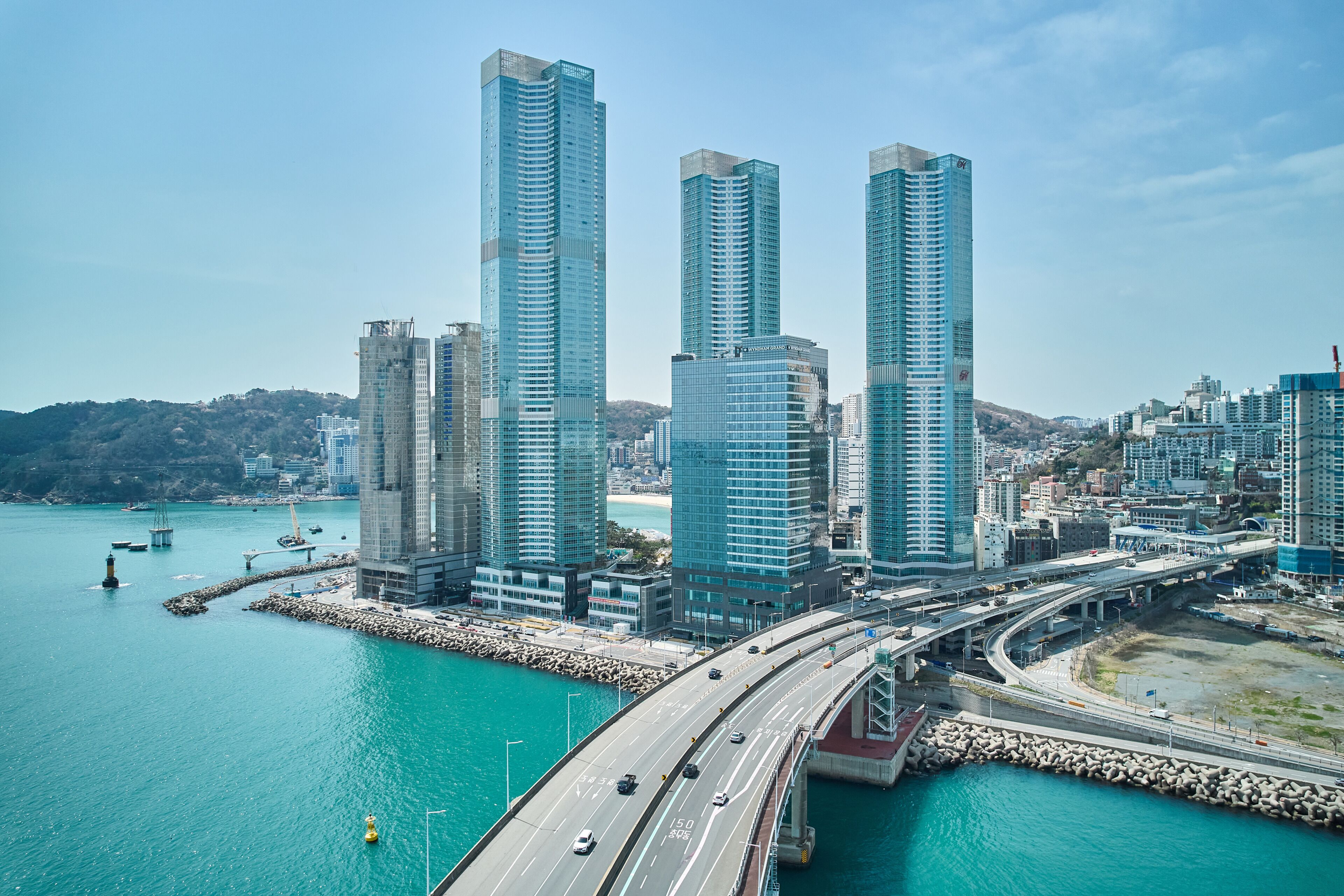 Un paisaje urbano costero con modernos rascacielos, un puente y un puerto deportivo.