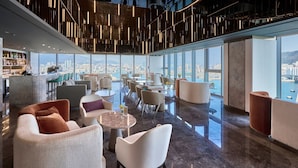 A modern lounge with a city view, featuring a bar area, seating arrangements, and a high ceiling with hanging lights. - Wyndham Grand Busan Ijin (Busan)