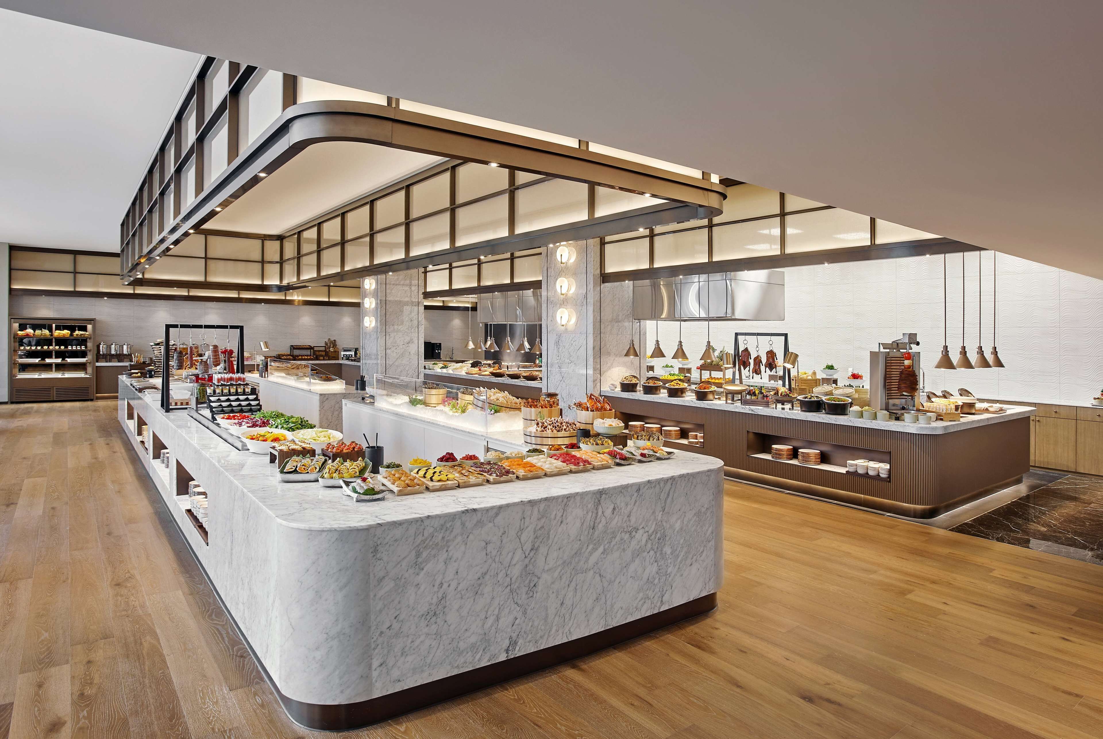 A modern hotel lobby with a marble reception desk, a large buffet area, and a spacious layout with wooden flooring and a high ceiling.