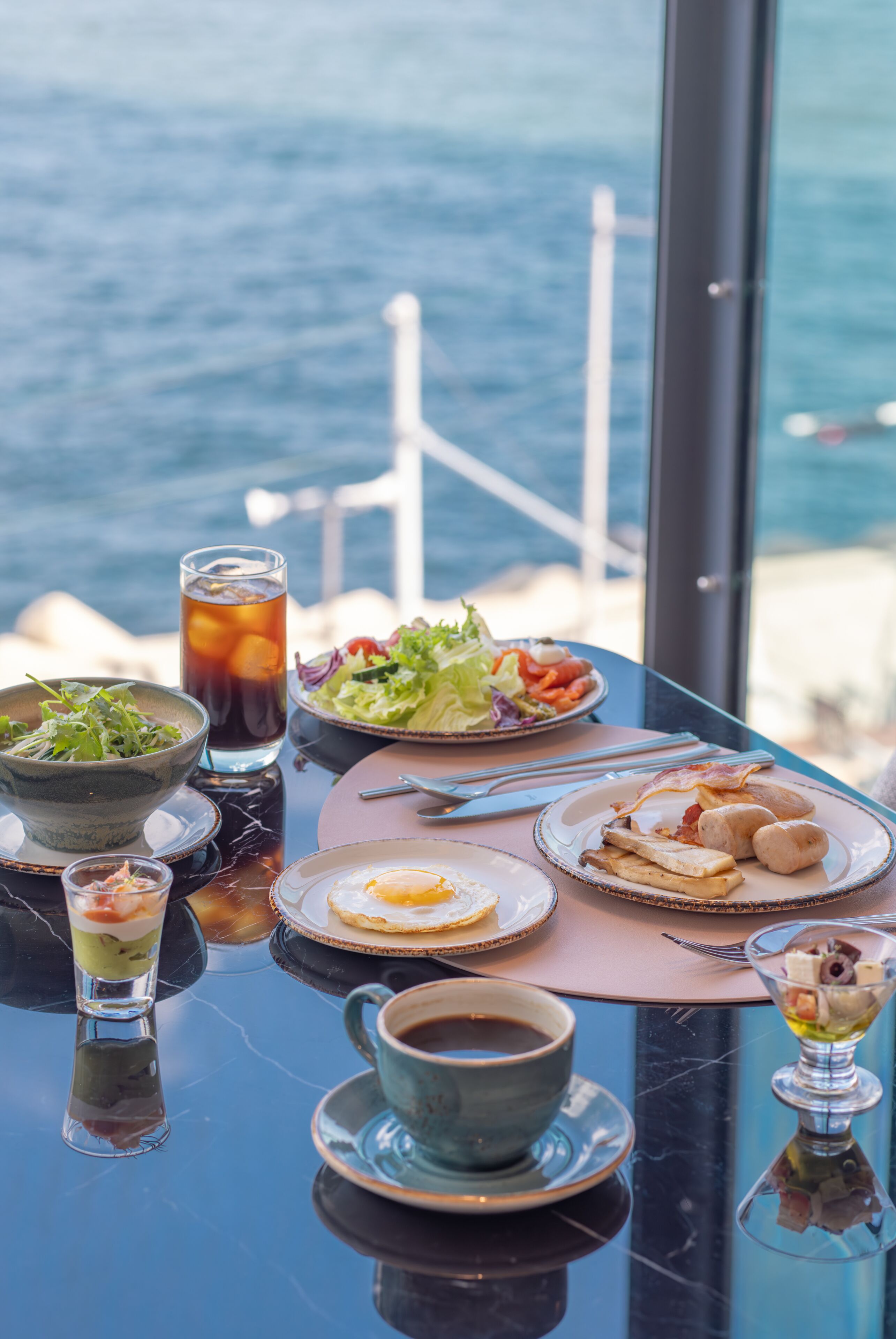 A table set with various dishes and drinks, overlooking a body of water.