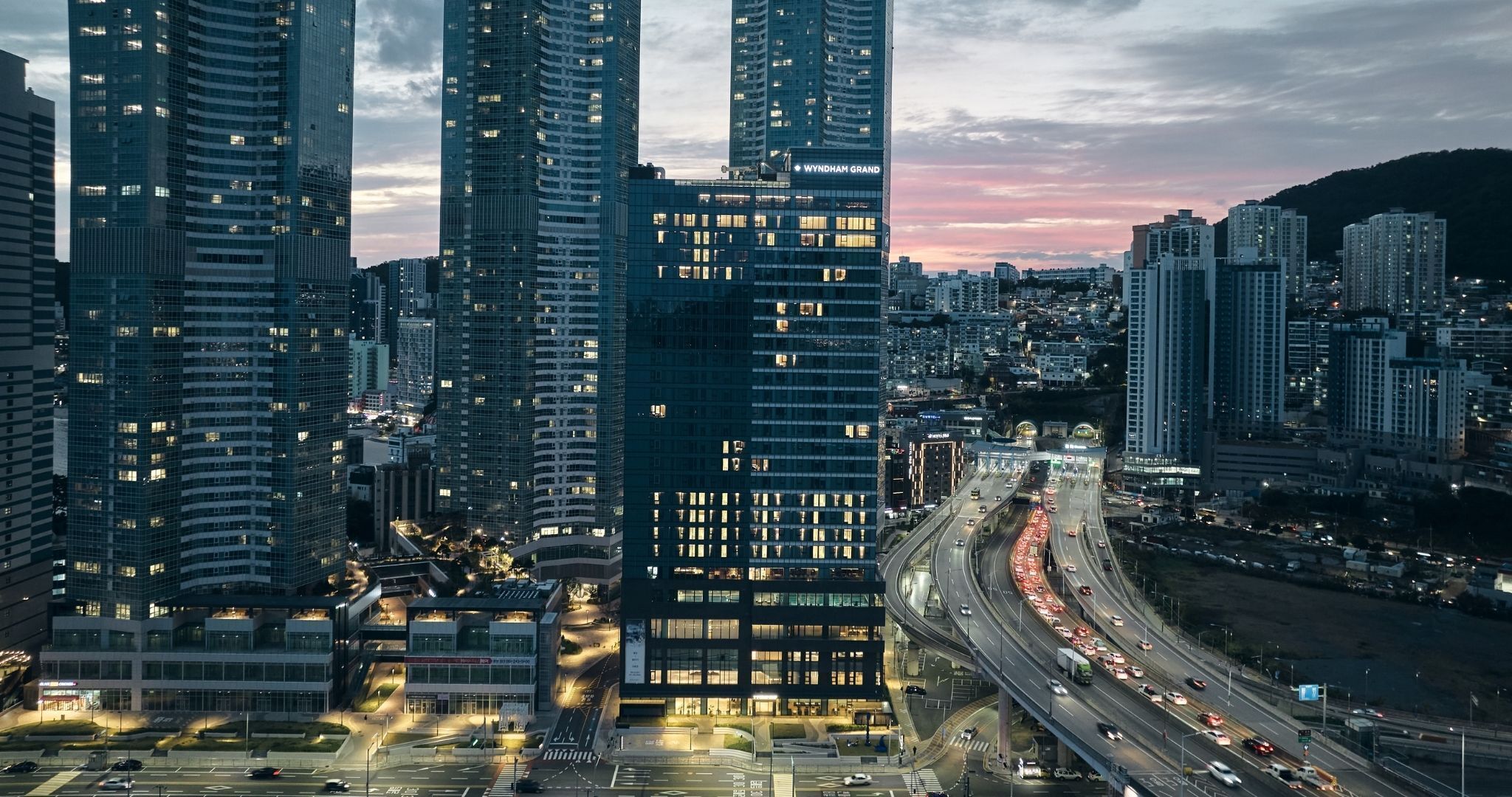 Un edificio de gran altura con varios pisos, rodeado de otros edificios altos, y una autopista concurrida llena de vehículos.