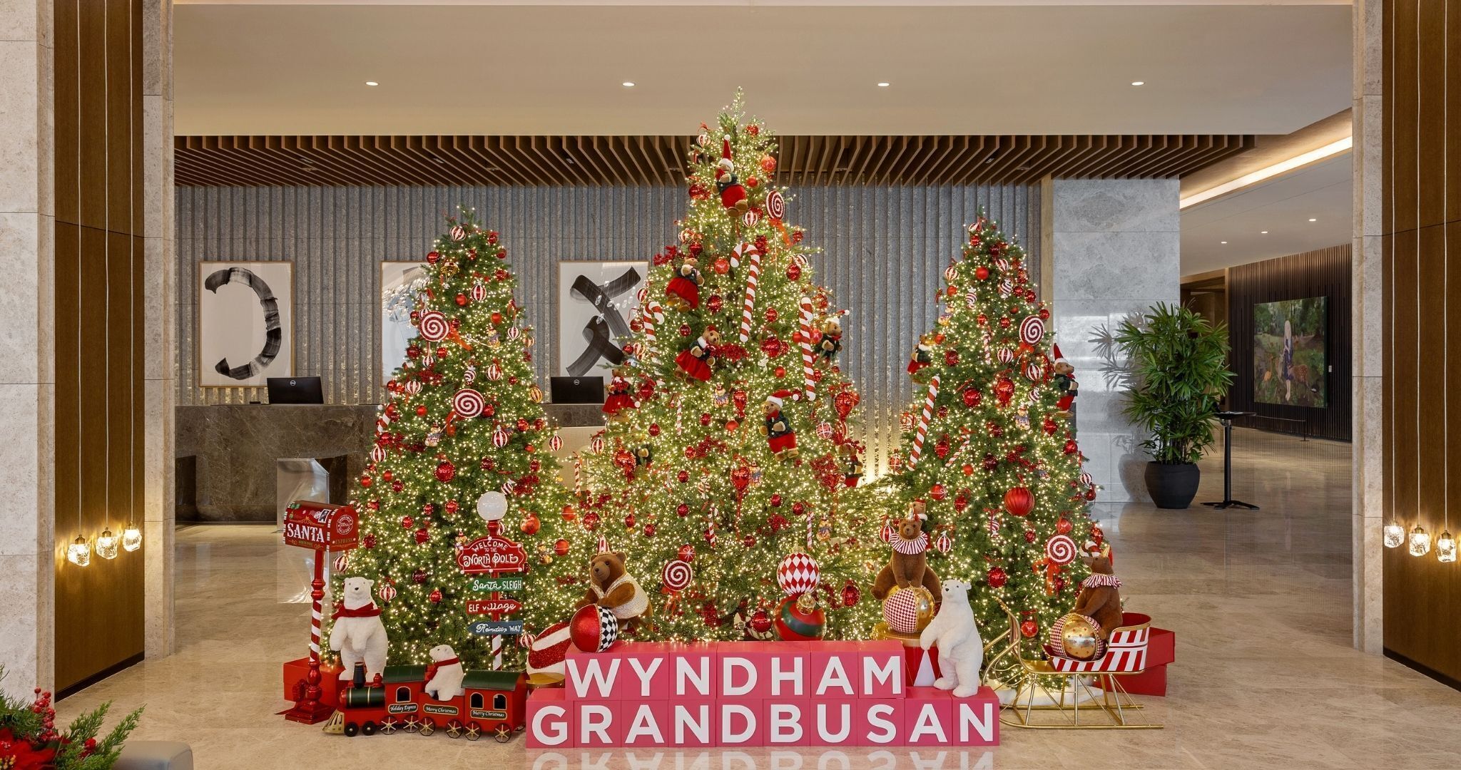 A grand lobby with three decorated Christmas trees, a reception desk, and a large sign reading "WYNDHAM GRANDBUSAN".