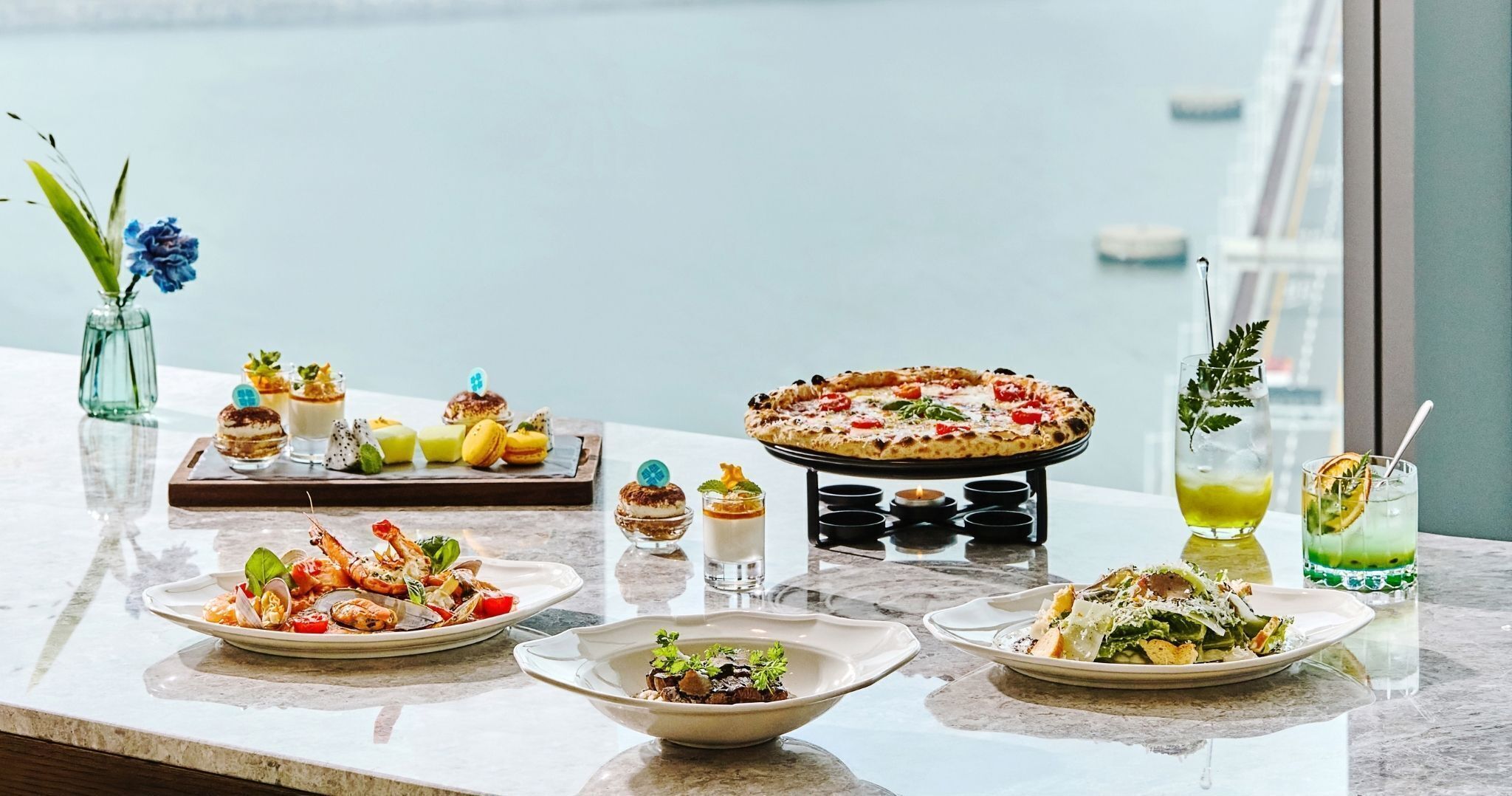 A variety of dishes and drinks on a table with a view of the sea.