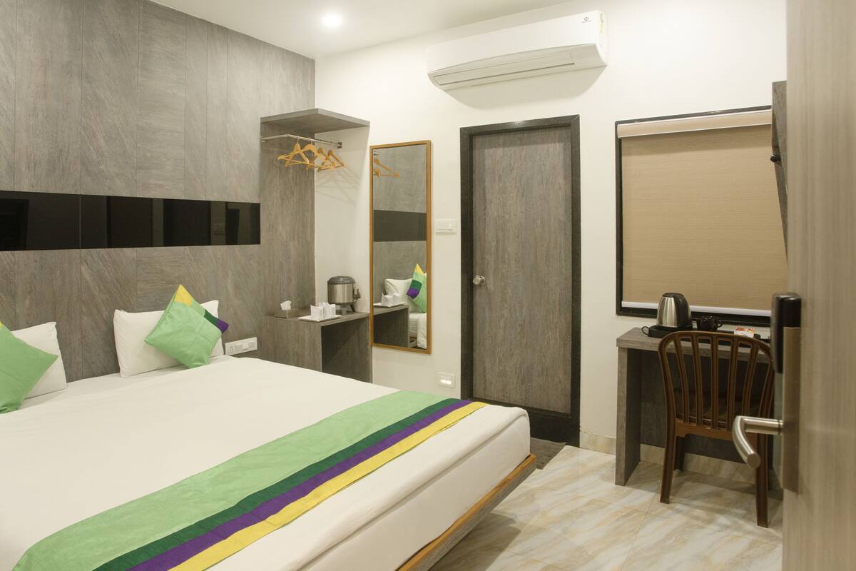 A modern hotel room with a large bed, a desk, a chair, and a wardrobe.