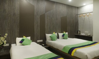 Habitación de hotel con dos camas, cada una con ropa de cama blanca y almohadas verdes, una mesita de noche pequeña con un teléfono y una taza, y un espejo en la pared.
