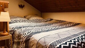 A bedroom with a sloped ceiling, a wooden bed frame, patterned bedding, and a bedside lamp. - Jolie Appartement Avec une Chemine,balcon Expose sud Avec Magnifique vue (Les Deux Alpes)