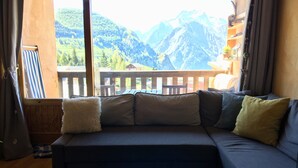 A living room with a sofa, pillows, and a view of mountains through a large window. - Jolie Appartement Avec une Chemine,balcon Expose sud Avec Magnifique vue (Les Deux Alpes)