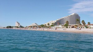 A coastal hotel with multiple white buildings, a sandy beach, and palm trees. - Studio Port Marina Baie des Anges (Villeneuve-Loubet)