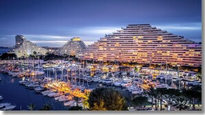 A marina with multiple boats docked, a large hotel with multiple floors, and a clear sky. - Studio Port Marina Baie des Anges (Villeneuve-Loubet)