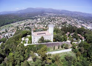 An aerial view of a historic castle surrounded by dense greenery and a town in the background.