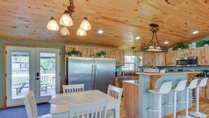 Una cocina con armarios de madera, un refrigerador de acero inoxidable, un microondas y una zona de bar con taburetes blancos.