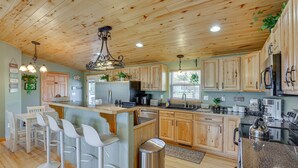 Una cocina con armarios de madera, una isla central con taburetes de bar, electrodomésticos de acero inoxidable y una lámpara colgante.