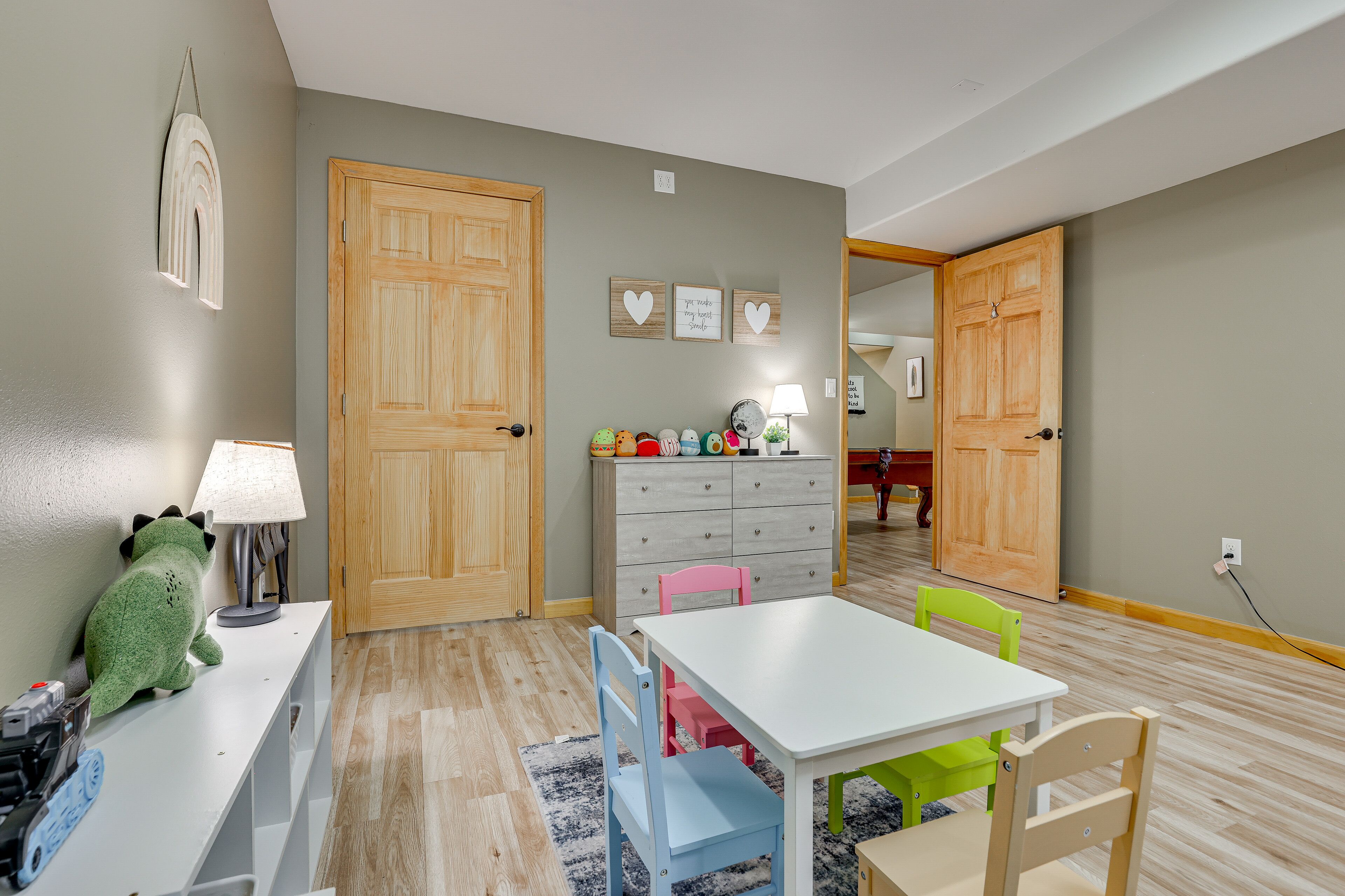 A room with a white table, two chairs, a lamp, a dresser, and a green plush toy.