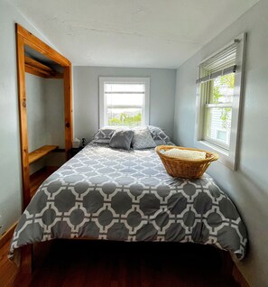A bedroom with a bed, two windows, a wooden ladder, and a wicker basket on the bed. - Buttermilk Bay view, 2 bd room, beach & large deck (Bourne)