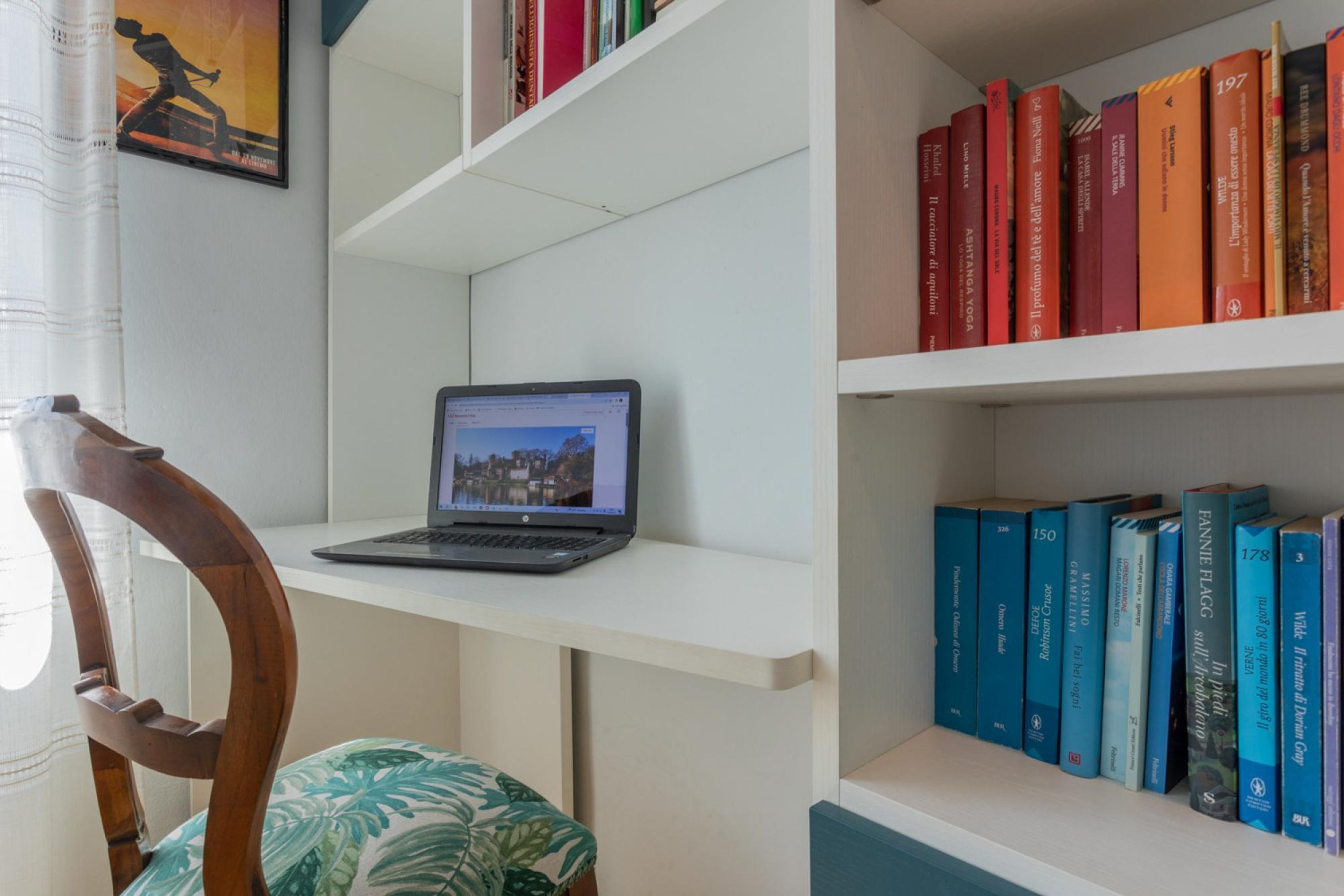 A bookshelf with books, a laptop on a shelf, and a chair with a patterned cushion.