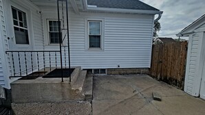 A white house with a front porch, a small window, and a wooden fence in the background.