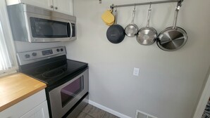 A compact kitchen with a microwave, stove, oven, and pots hanging on the wall.