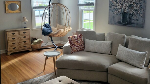 A living room with a hanging chair, a sofa, a small table, a dresser, and a painting on the wall.