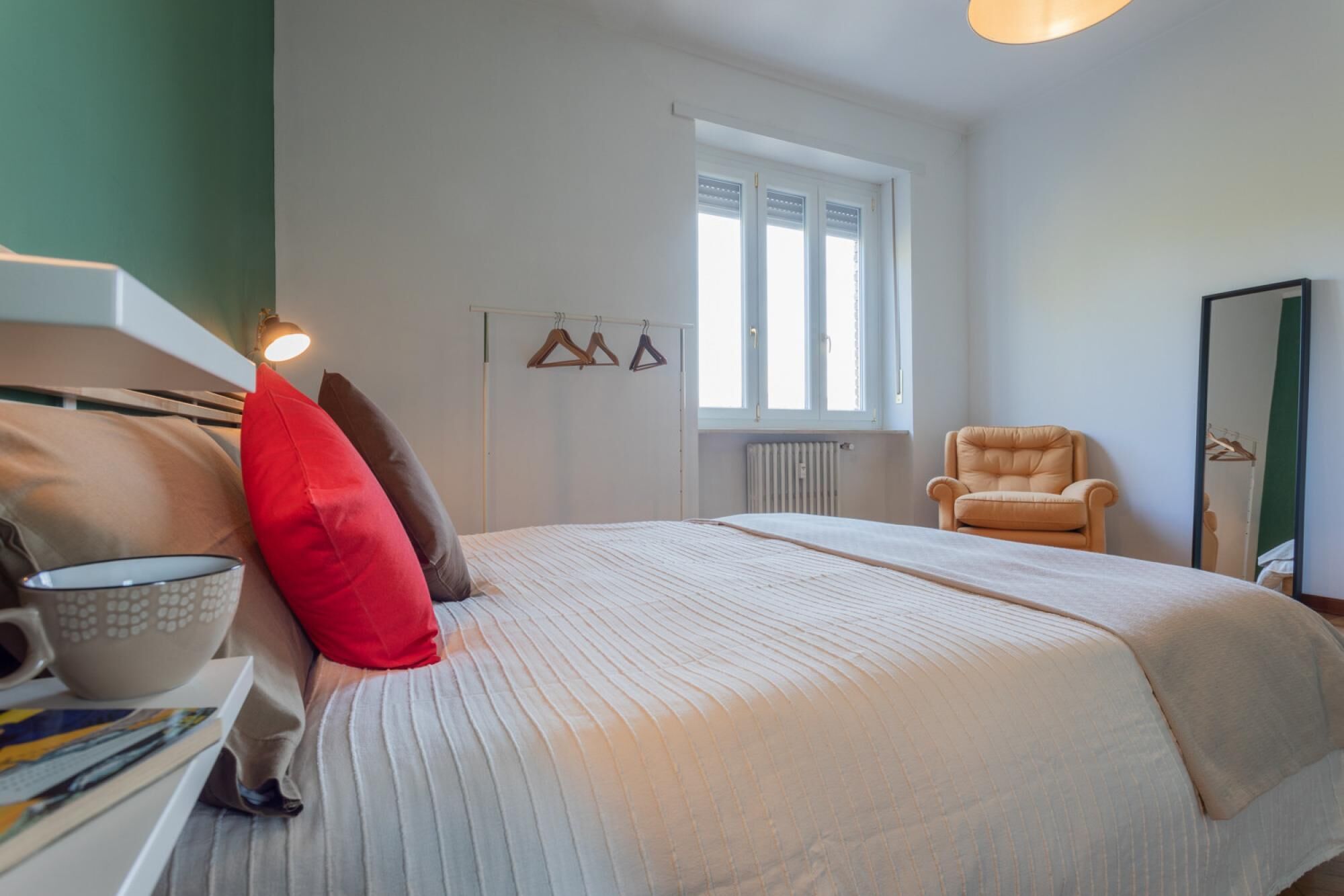 A bedroom with a bed, a chair, a radiator, and a window.