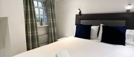 A modern hotel room with a large bed, a headboard with a light fixture, and a window with curtains.