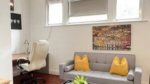 A modern living room with a grey sofa, two yellow cushions, a black coffee table with plants, a white office chair, and a large window with a cityscape painting above it. - Stunning 2-bed Apartment in Maidstone (Maidstone)