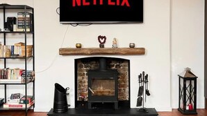 A living room with a fireplace, a bookshelf, and a TV mounted above the fireplace displaying "NETFLIX". - Stunning 2-bed Apartment in Maidstone (Maidstone)