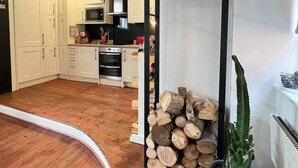 A modern kitchen with white cabinets, a built-in oven, and a microwave. There is a wooden log display and a potted cactus plant. - Stunning 2-bed Apartment in Maidstone (Maidstone)