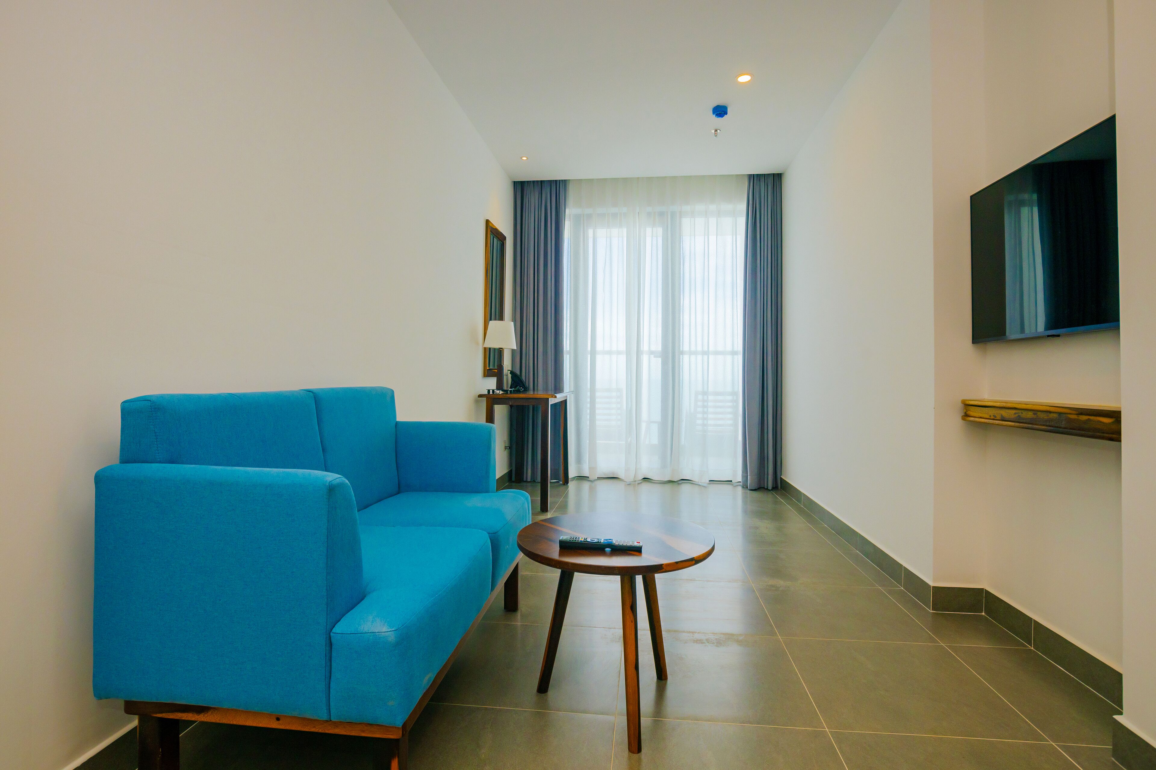 Una sala de estar moderna con un sofá azul, una mesita redonda y un televisor de pantalla plana montado en la pared.