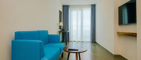 A modern living room with a blue sofa, a small round table, and a flat-screen TV mounted on the wall.