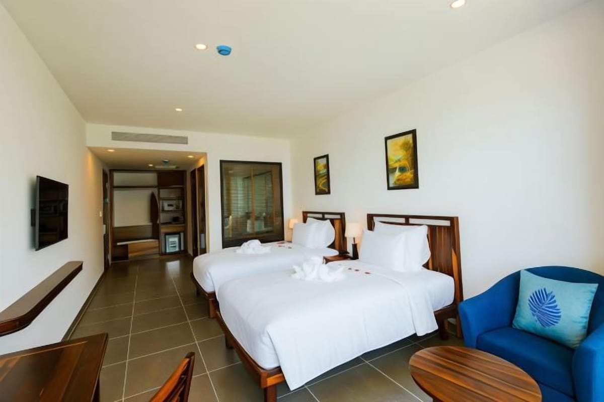A hotel room with two beds, a seating area with a blue sofa, a wooden coffee table, and artwork on the walls.