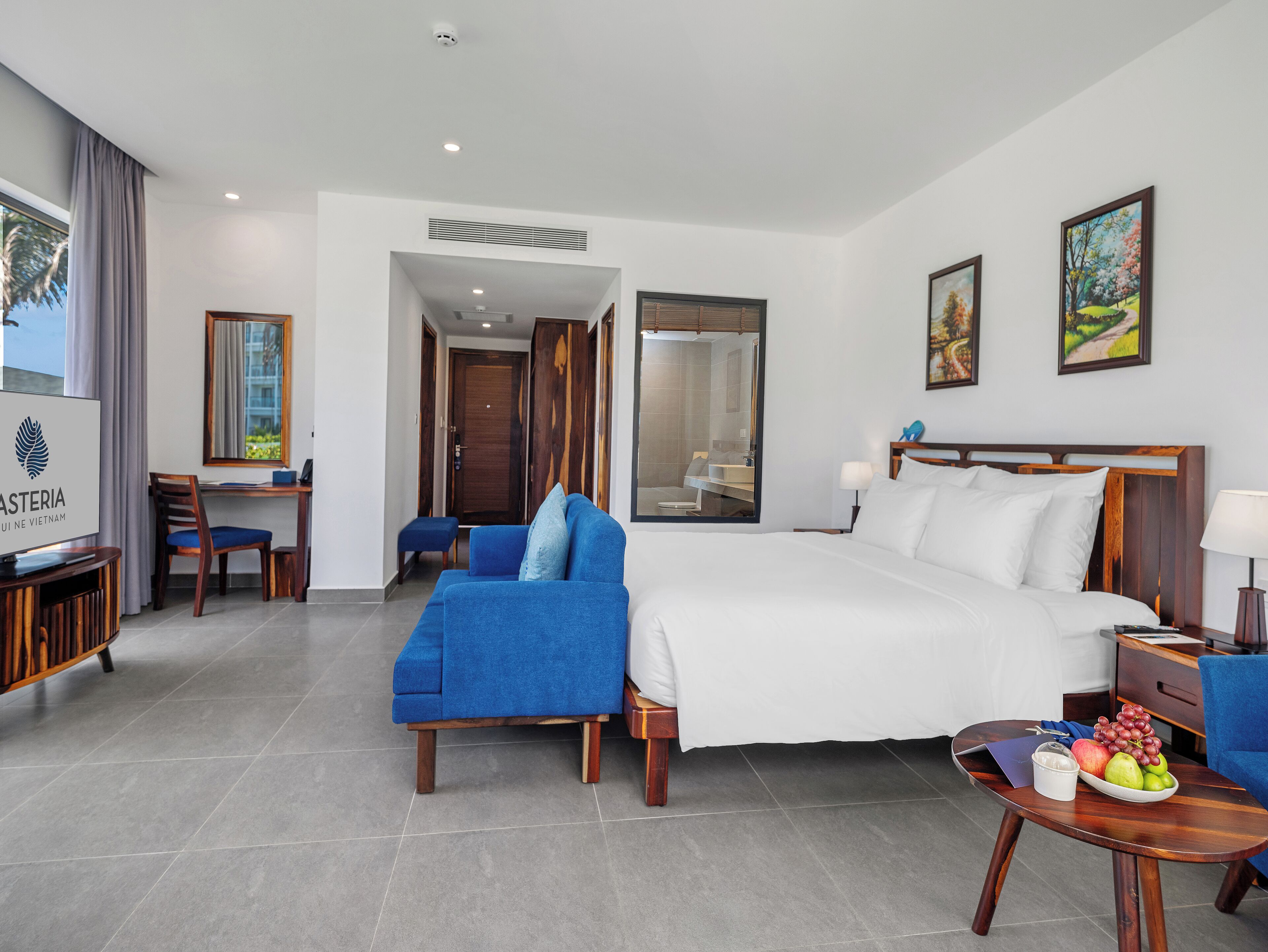 Una habitación de hotel con cama, escritorio, silla, televisión y una mesa de comedor con frutas.