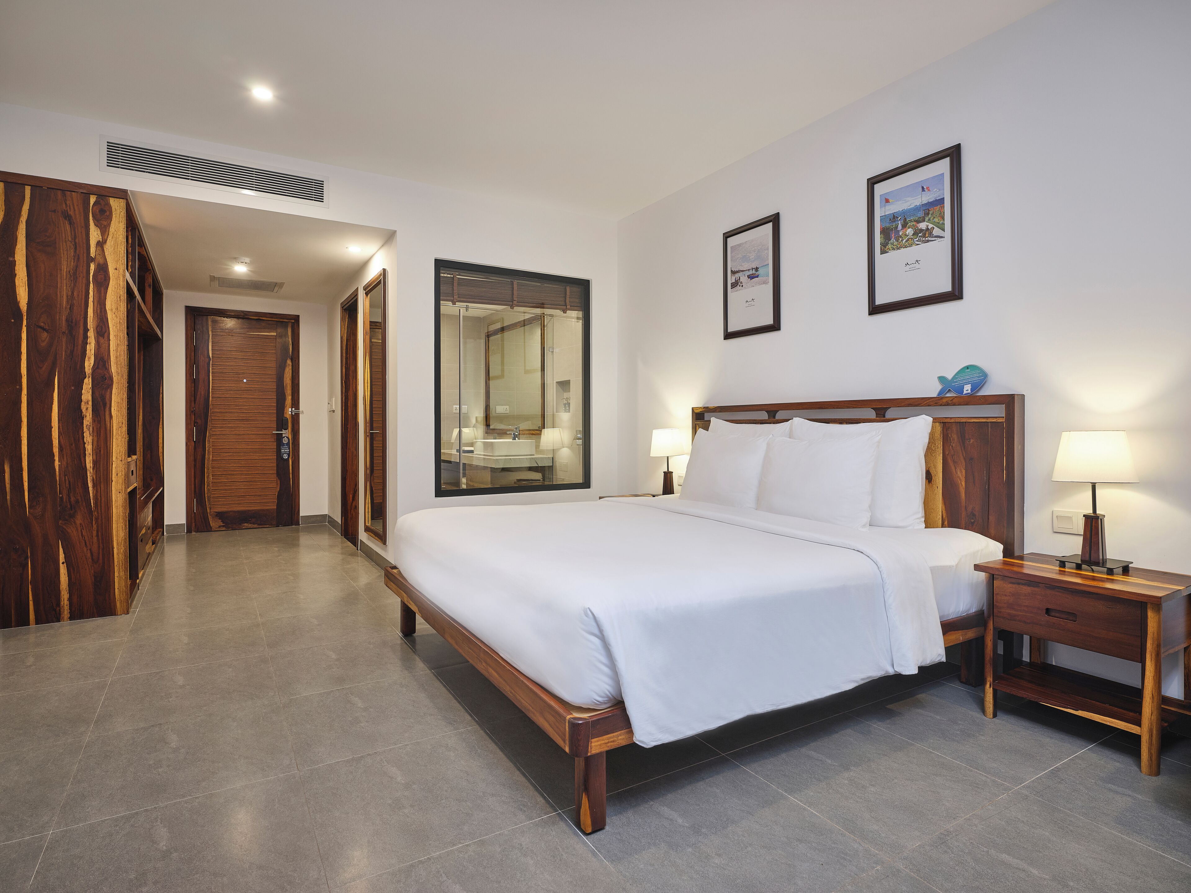 Habitación de hotel con una cama grande, cabecera de madera, dos mesitas de noche con lámparas, un espejo grande y un armario de madera.