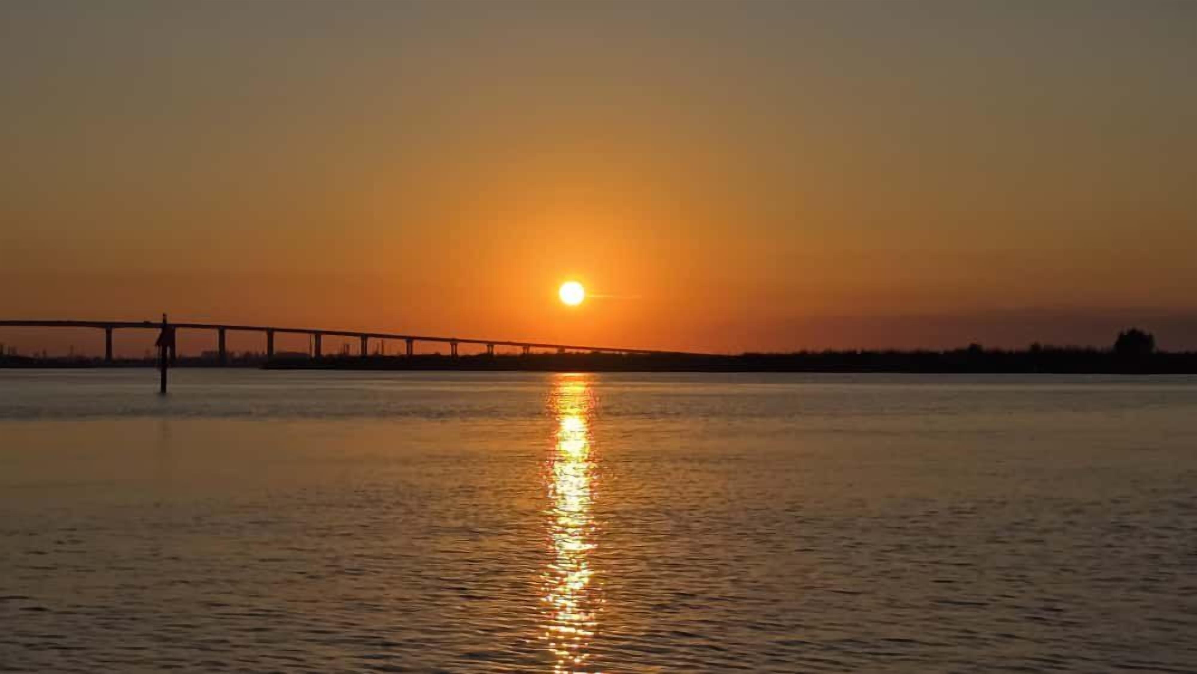 A sunset over a body of water with a bridge in the distance.