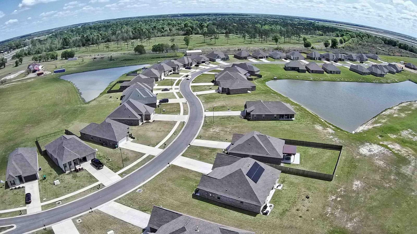 Zona residencial con casas dispuestas en una distribución curva, conectadas por caminos, rodeada de campos verdes y cuerpos de agua.