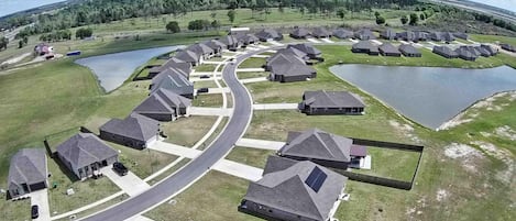 Zona residencial con casas dispuestas en una distribución curva, conectadas por caminos, rodeada de campos verdes y cuerpos de agua.