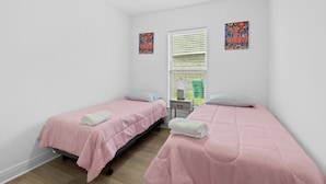 A room with two single beds, a small bedside table, a window with blinds, and two wall-mounted artworks. - Hideaway Spot Where Southern Charm Stays - LT7950 (Calcasieu Parish)