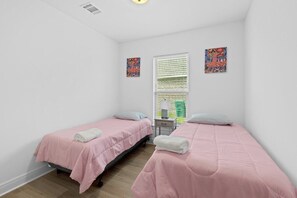 Una habitación con dos camas individuales, una mesita de noche, una ventana con persianas y dos obras de arte colgadas en la pared.