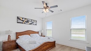 A bedroom with a wooden bed, a ceiling fan, a nightstand, a lamp, a rug, and two windows with blinds.